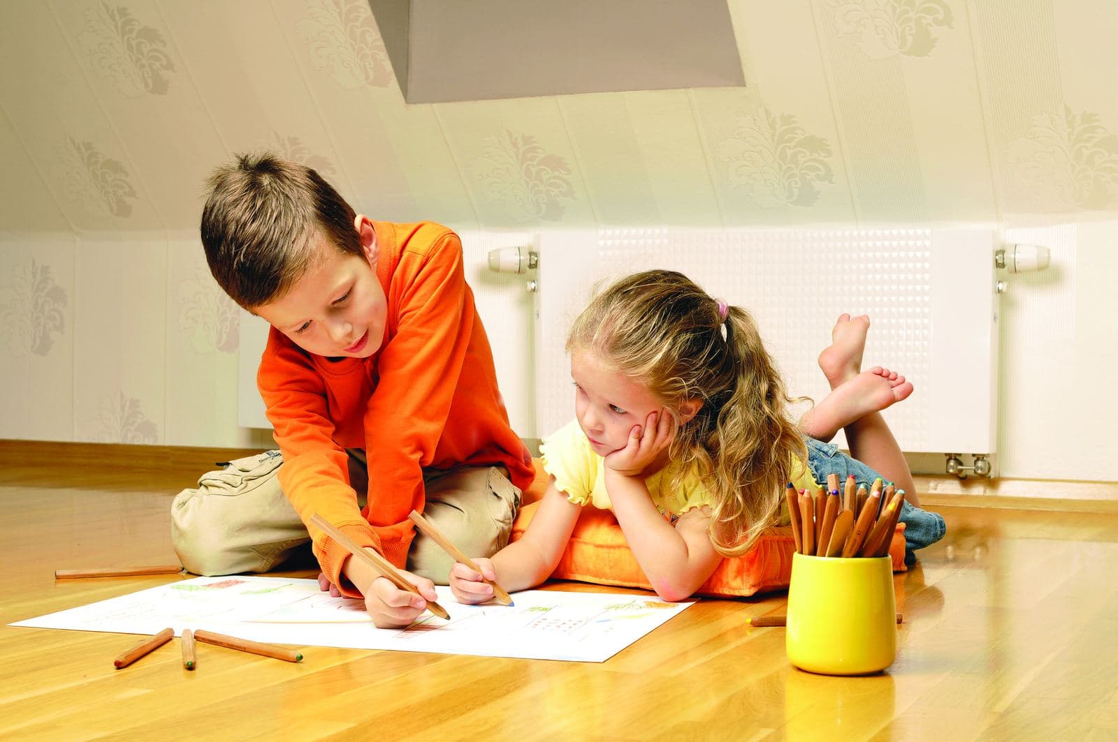 Two children drawing on the floor of a warm room